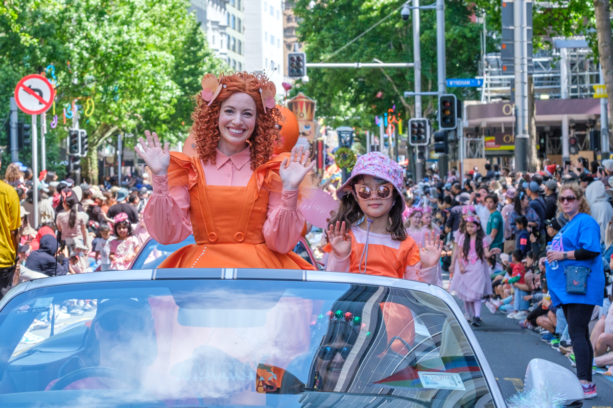 Emma Memma dressed in orange in a car for Santa Parade.