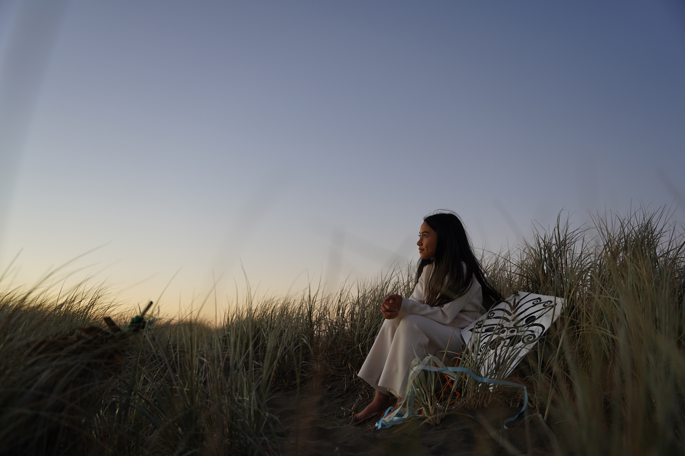 A young girl sitting next to a Māori kite during early dawn hours. 