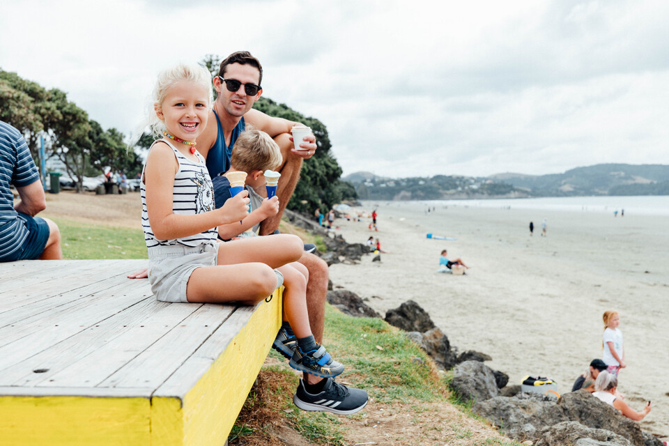 A father and his kids eating ice cream on a boardwalk by the beach. 