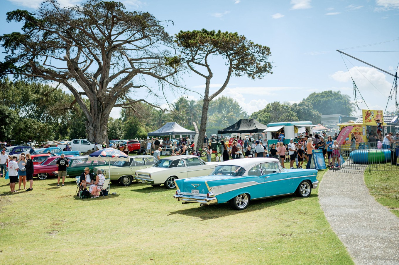 Classic cars parked up at iconic community day event with lots of stalls and eventgoers in the background.