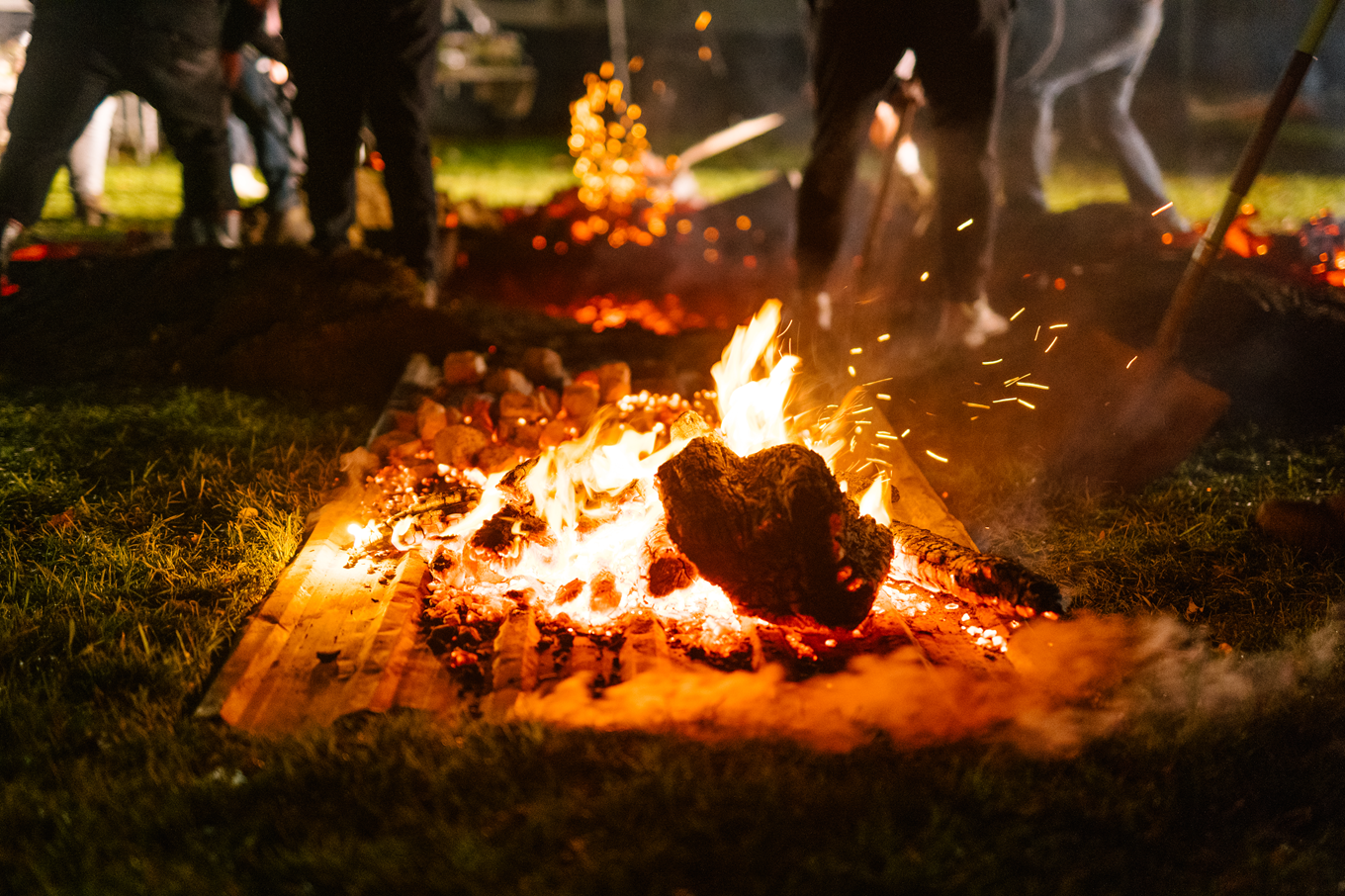A fire burning while men dig a pit for a hangi or underground oven. 