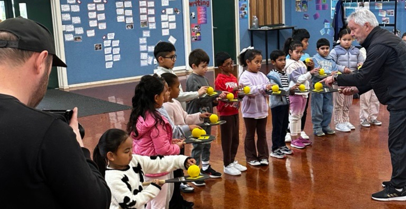 Primary school children learning to balance tennis balls on table tennis bats