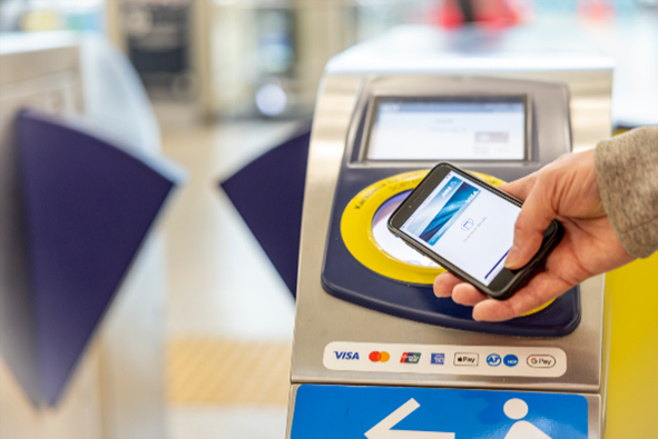 Hand holding a phone to the contactless payment terminal at an Auckland train station
