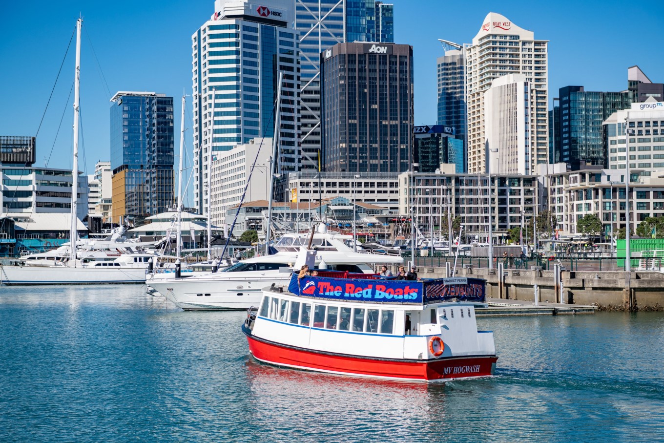 Red Boats ferry sailing past city waterfront. 