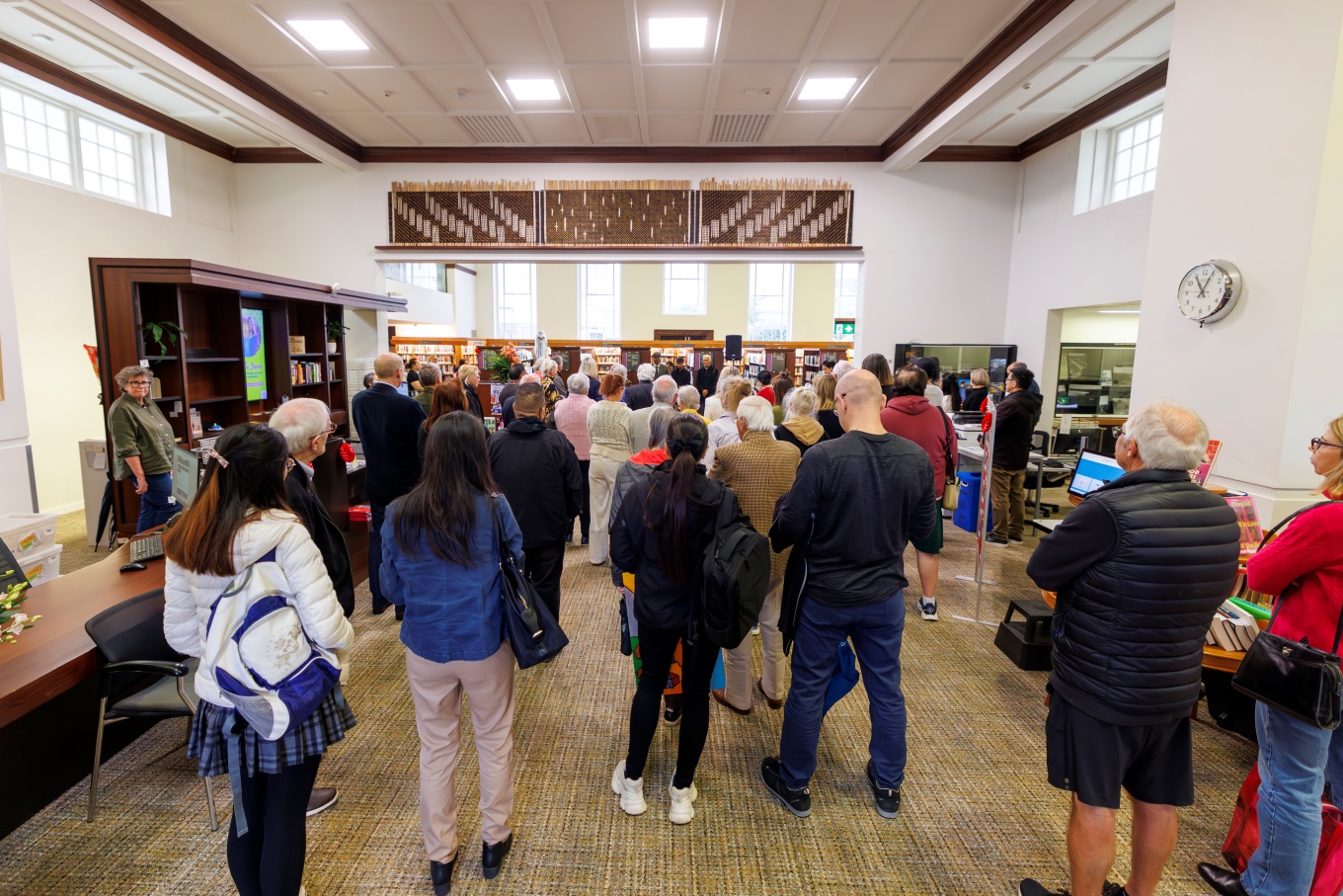 A crowd standing in a room with three woven artwork panels displayed on the wall.