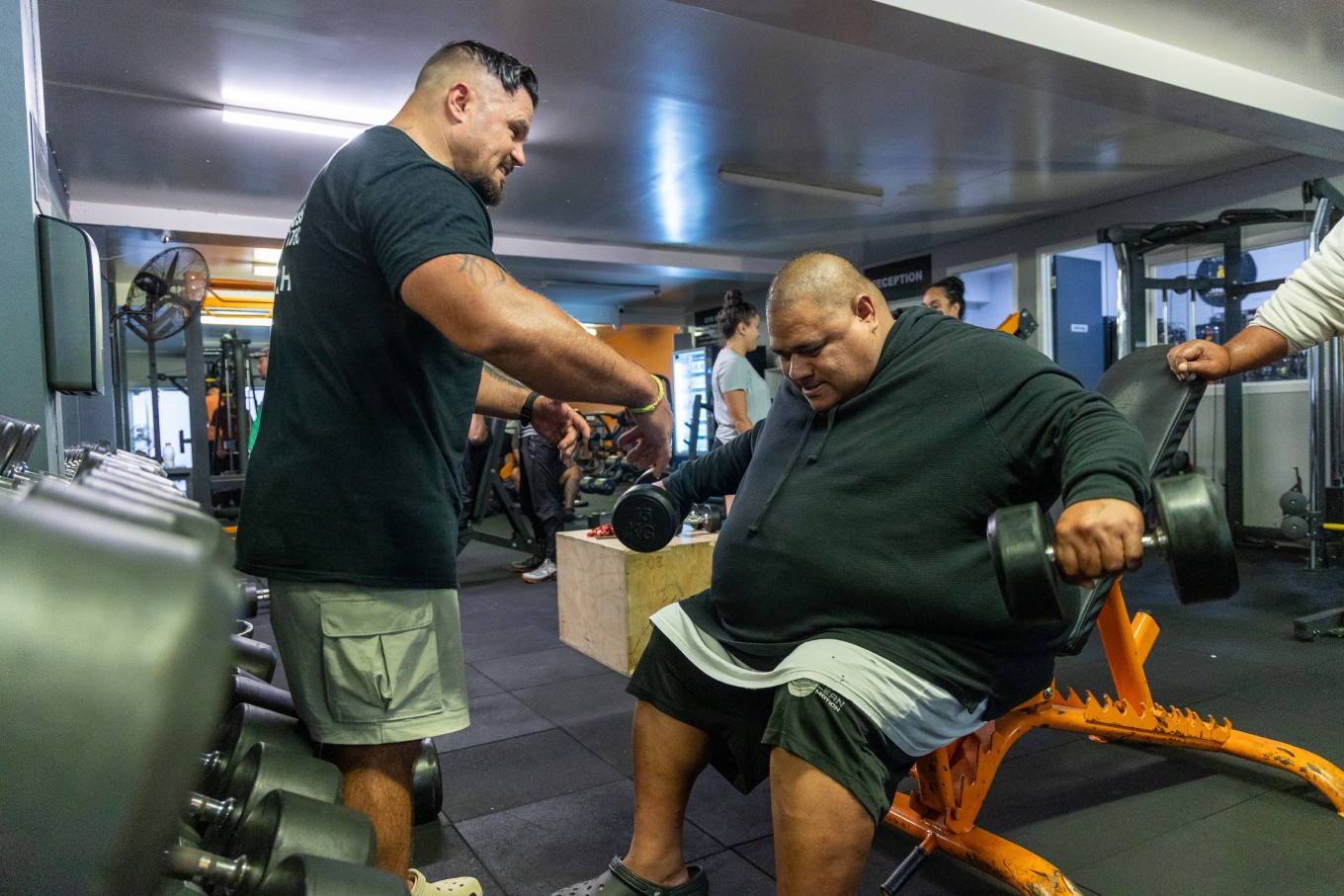 A fitness coach helping a man lift weights. 