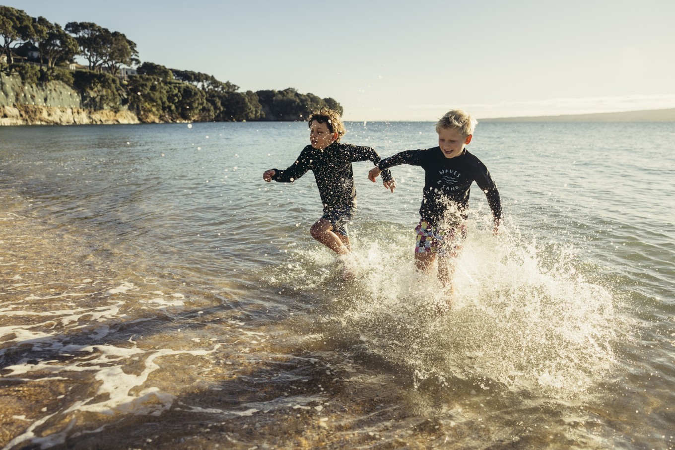 Two young boys running through the water. 