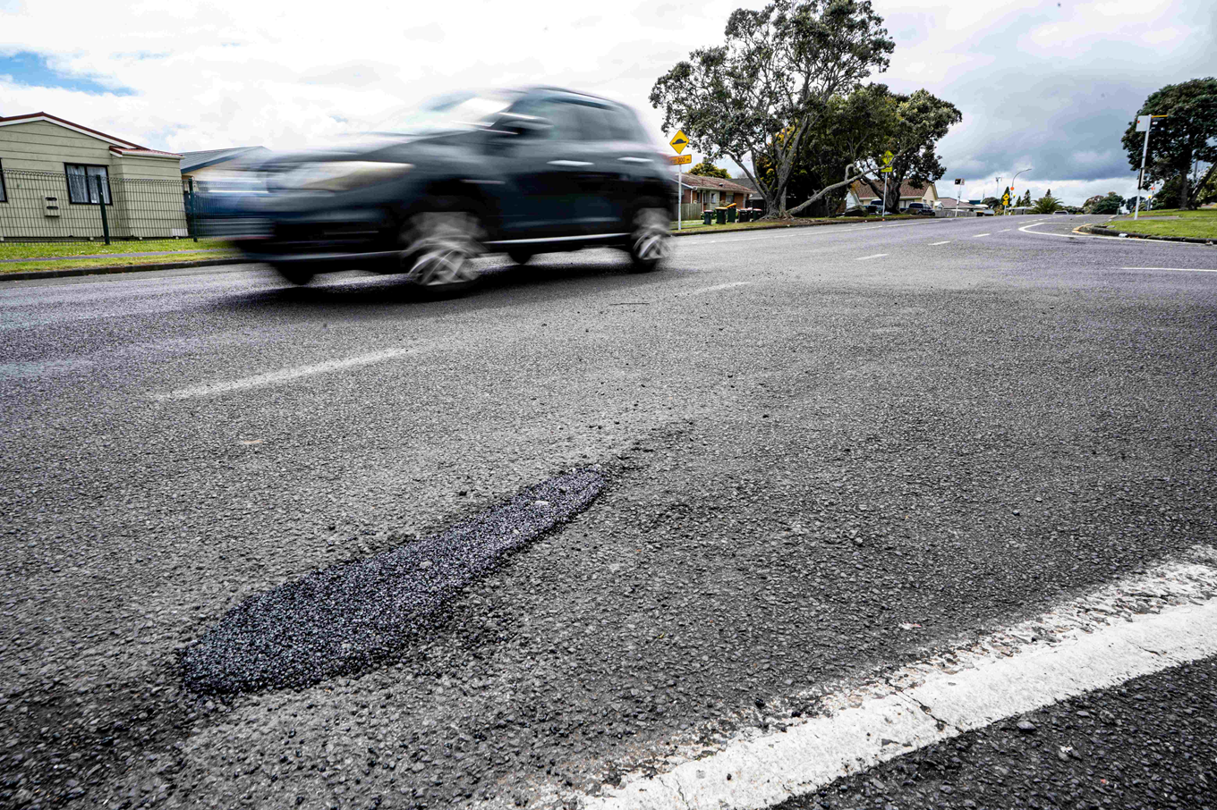 A pothole on the road with a car driving near by it. 