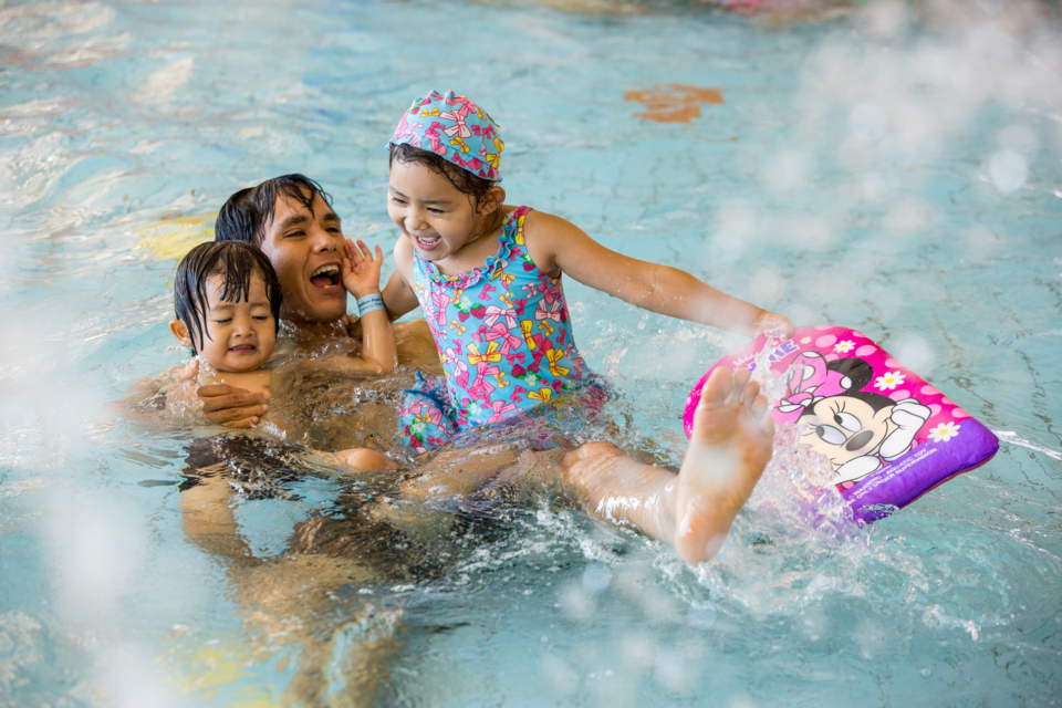 Father plays in the pool with his two young children.