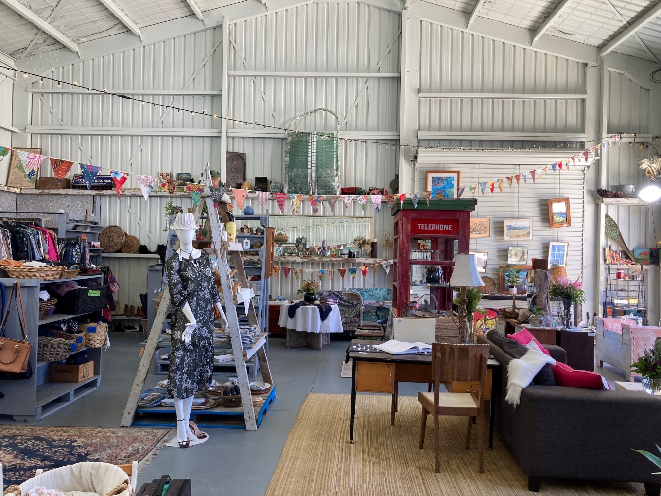 A second-hand store with furniture, shelves of items, clothing and a telephone box.