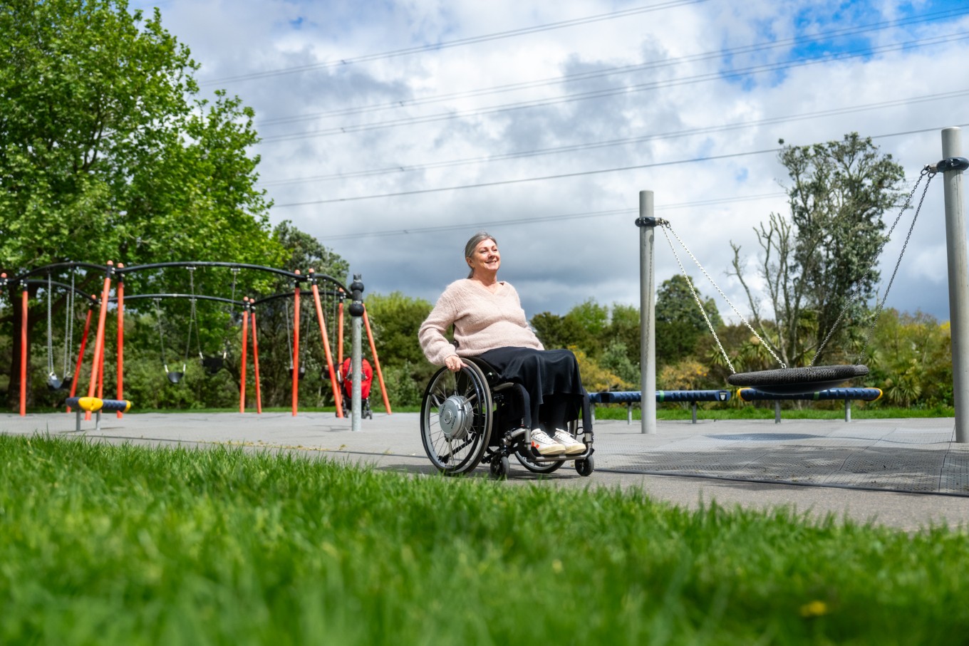 A woman in a wheelchair going past a playground. 