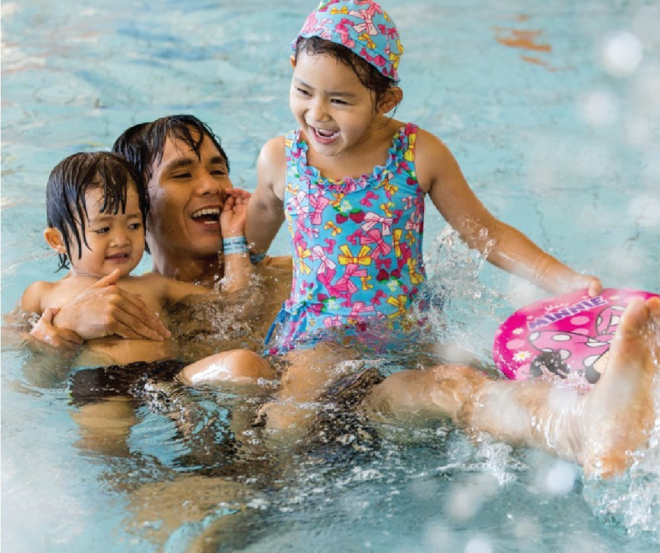 A father playing with his daughters in the pool. 