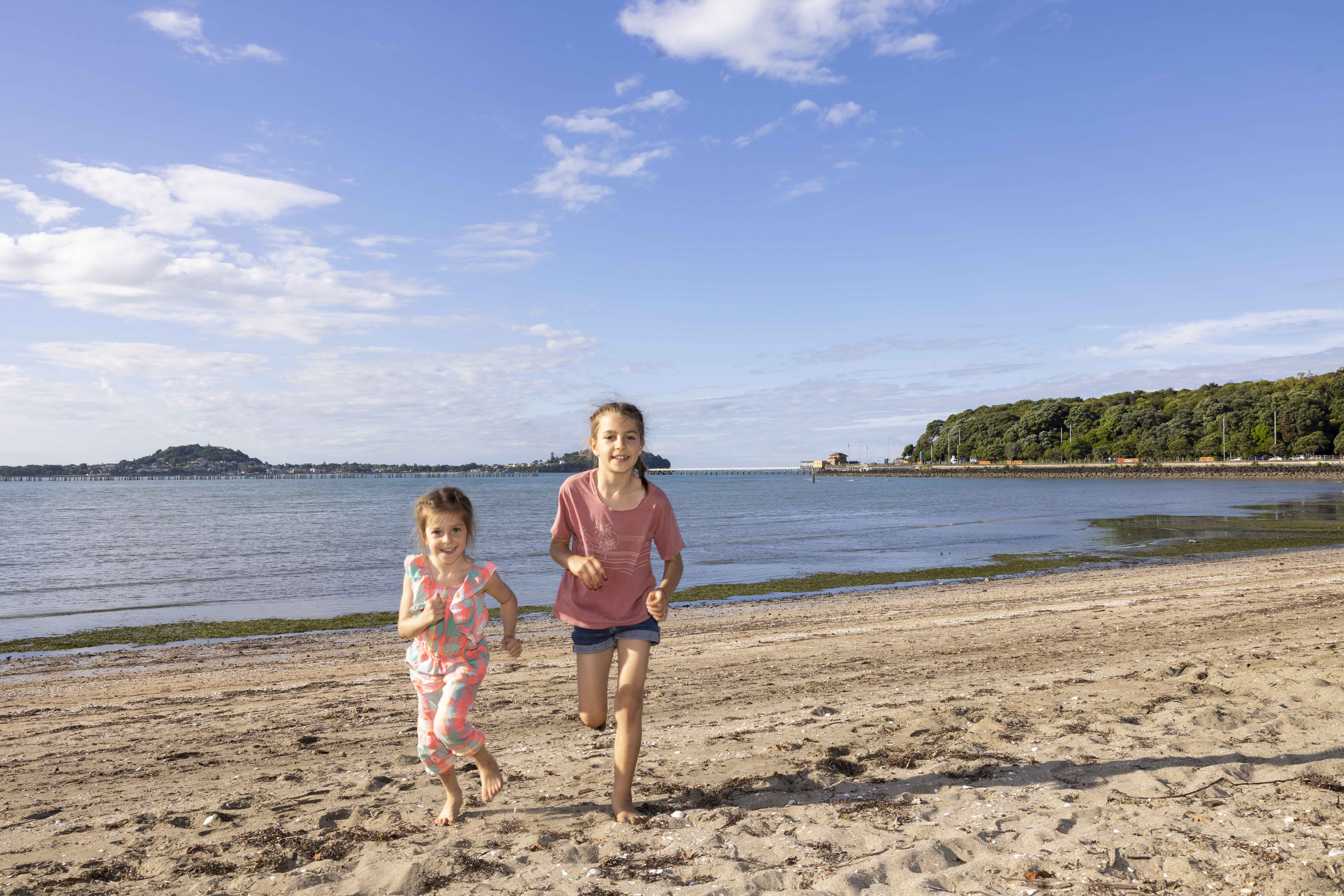 Two children running along Okahu Bay in Auckland