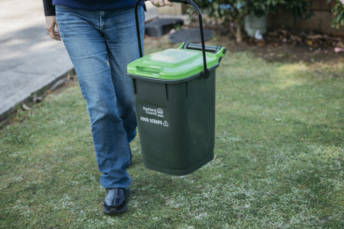 A person carrying their green bin down the street