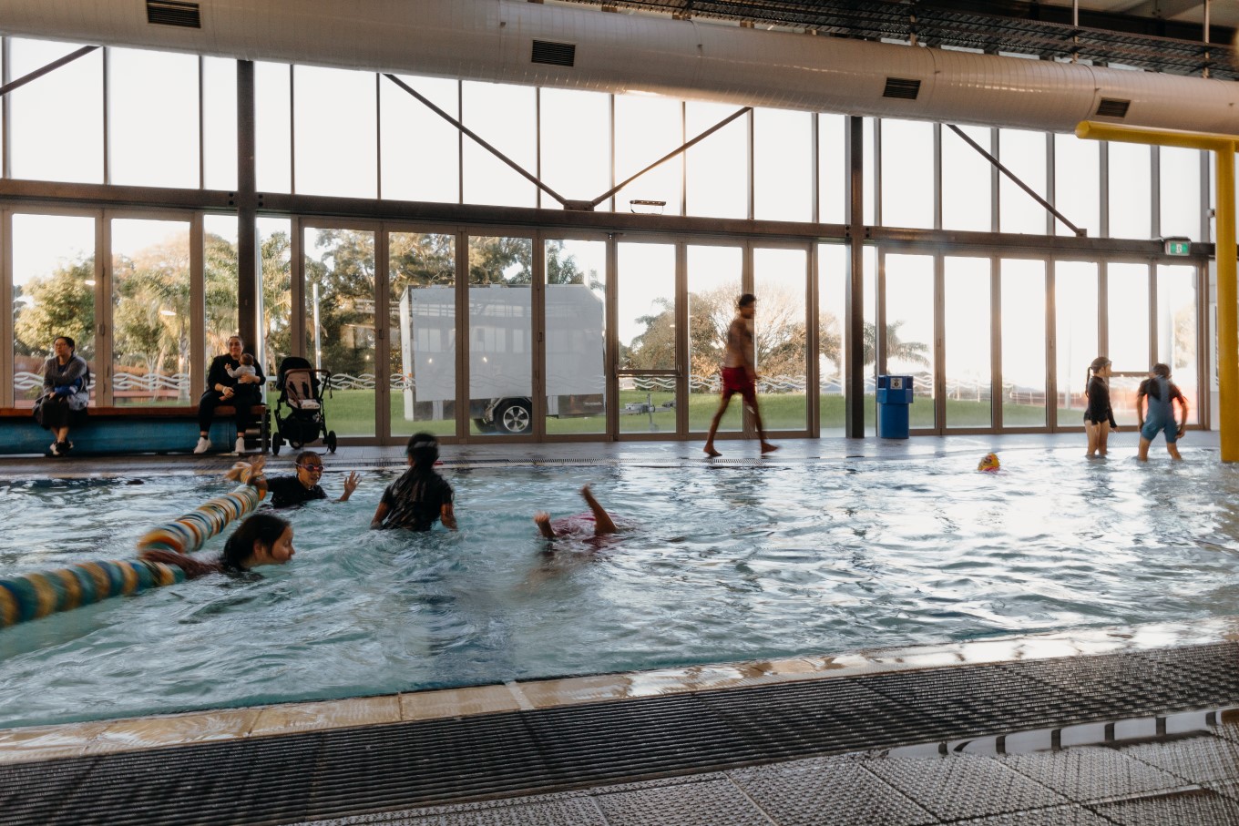 Parents watching their kids swimming in the pool. 