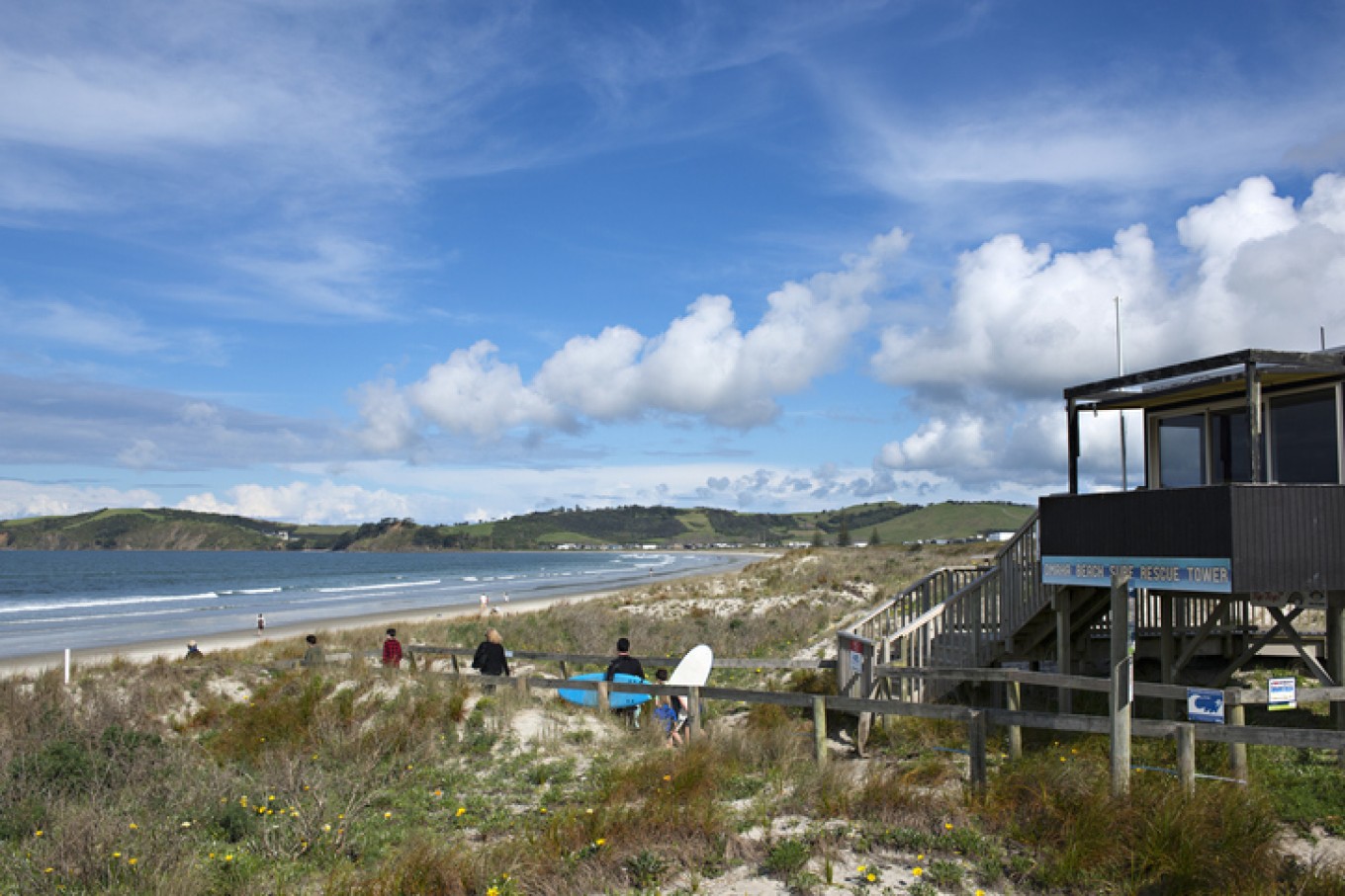 Surfers walking past a lifeguard building on the way to the beach. 