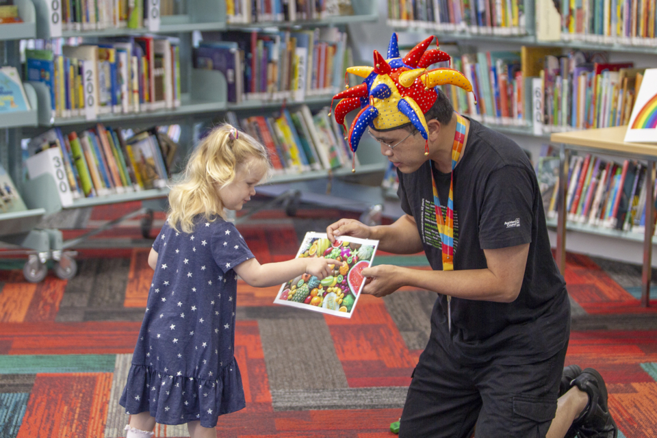 A male librarian showing a pictures book to a little girl in a library.