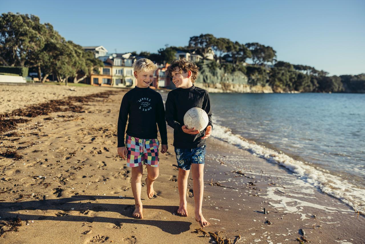 Two boys in swimming gear walking along the beach. 